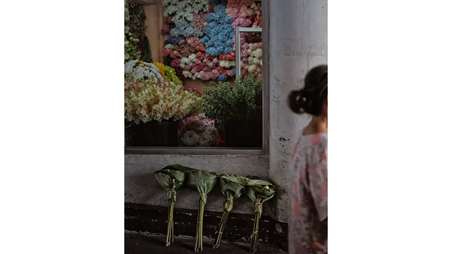 La vitrine d'un fleuriste, devant laquelle passe une femme vêtue d'un chemisier à fleurs