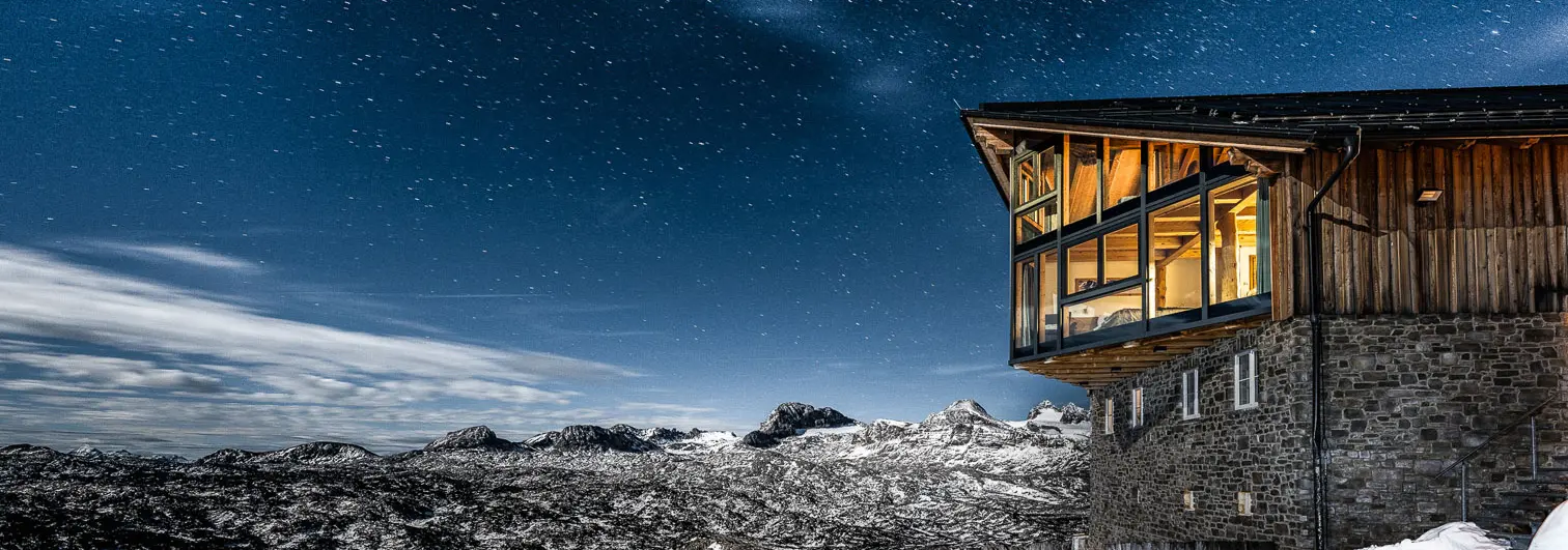Mountain lodge overlooking a snow-covered alpine landscape beneath a star-filled night sky.