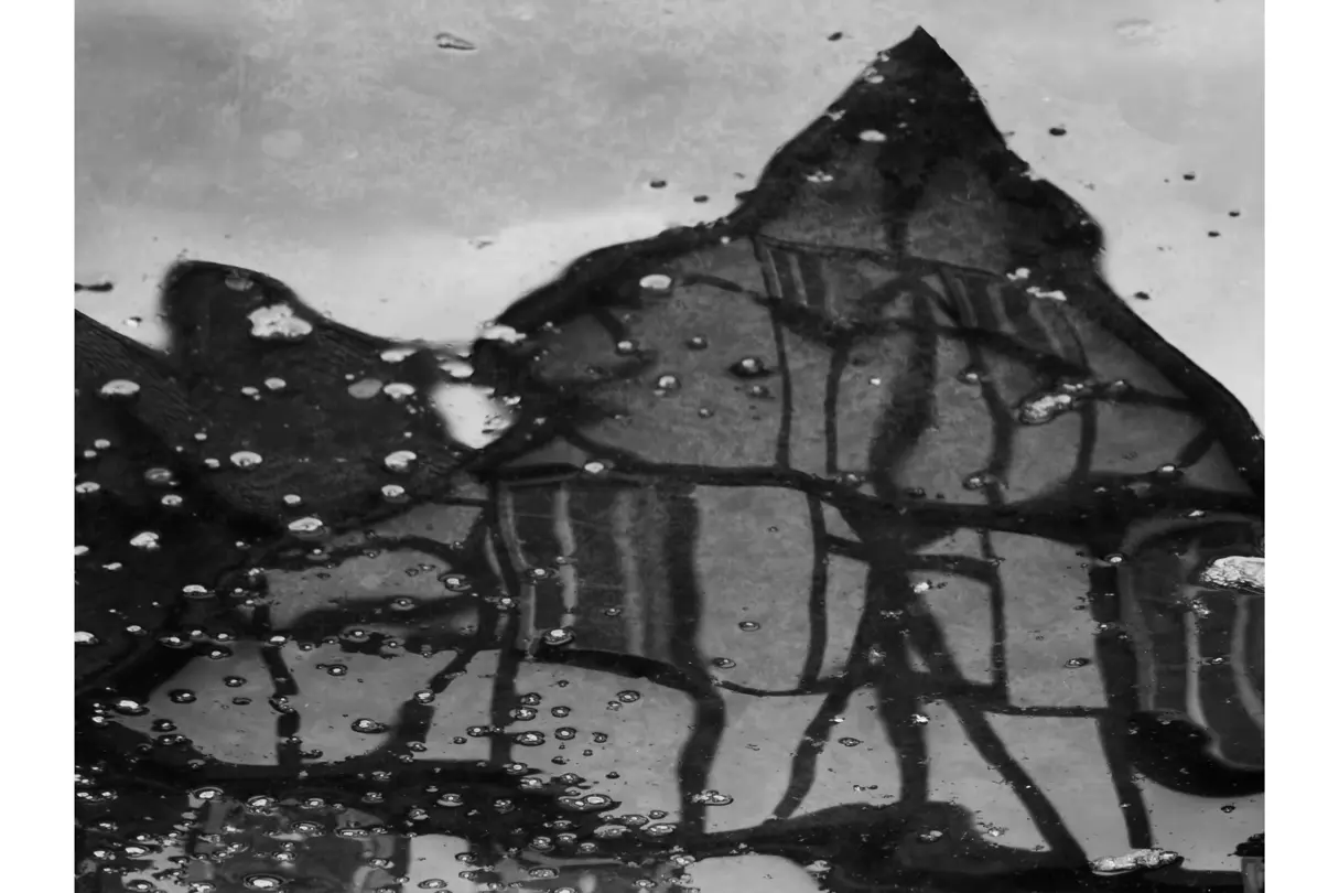 Reflection of historic buildings in a rain-covered puddle, creating an abstract black-and-white architectural composition.