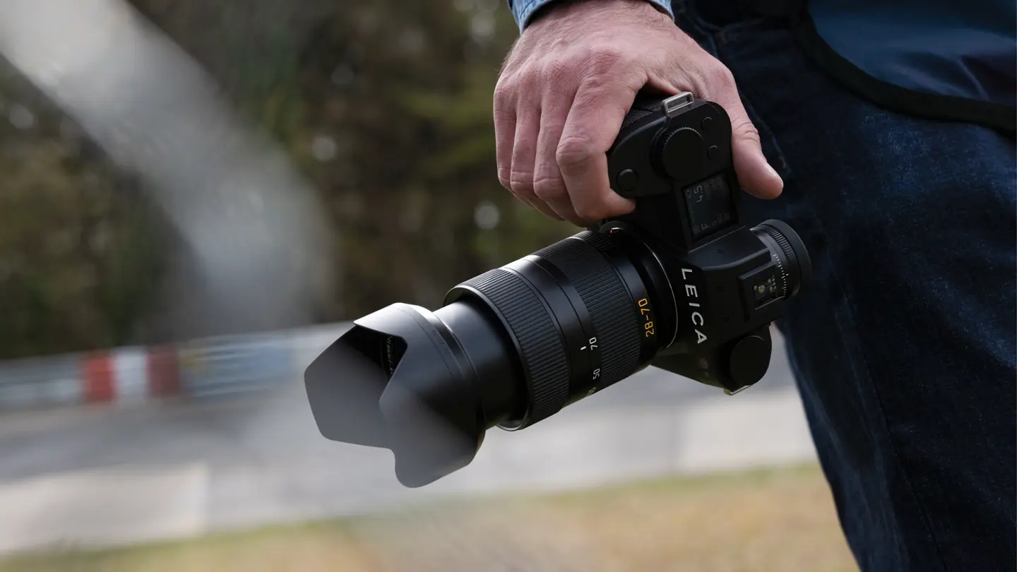 Person holding a Leica SL3-P camera with a telephoto lens outdoors.