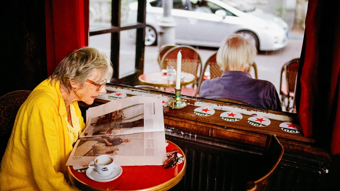 Colour Photograph of a woman reading a magazine at a cafe.