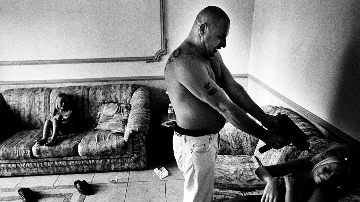 Black and white photograph of a man holding a weapon in a living space