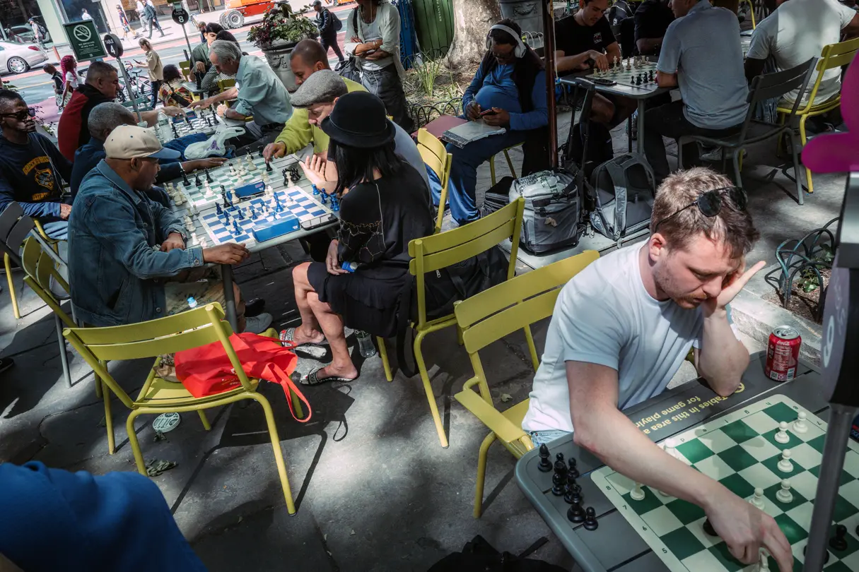 People playing chess at outdoor tables in a busy public park.