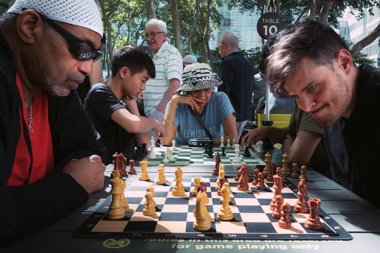 People playing chess at outdoor tables in a public park.