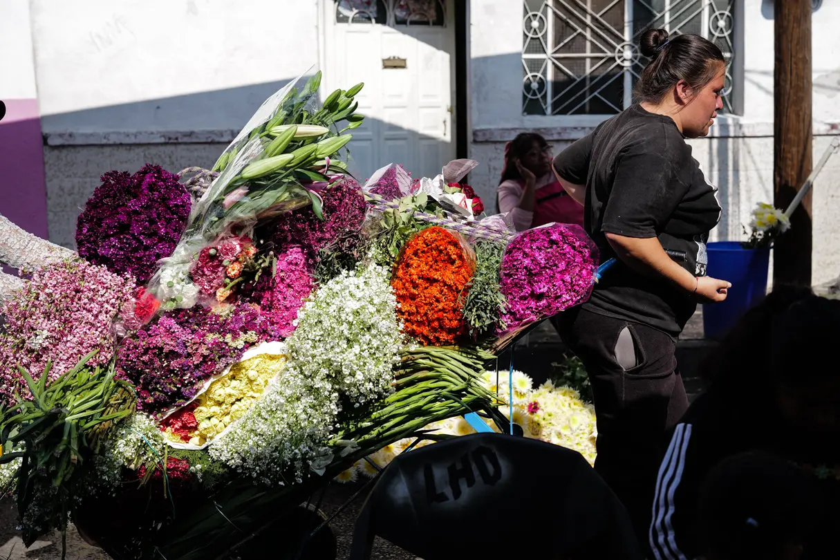 Flower vendor beside a cart overflowing with colorful bouquets, lilies and baby’s breath at an outdoor flower market in Mexico.