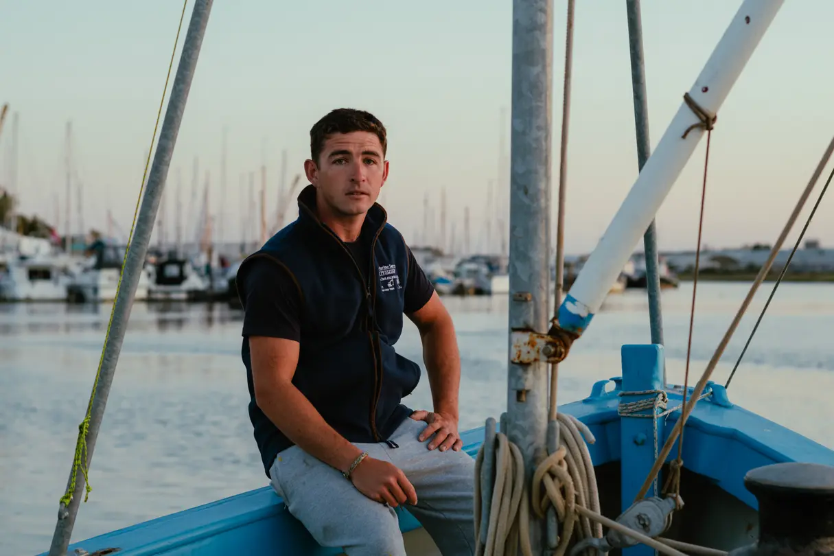 A young man is sitting on the edge of a sailboat