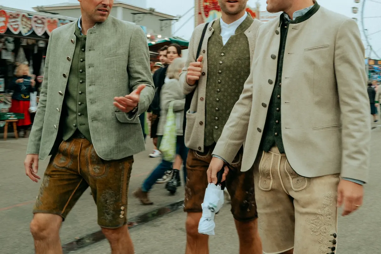 Three men in traditional Bavarian jackets and lederhosen walking through Munich Oktoberfest.