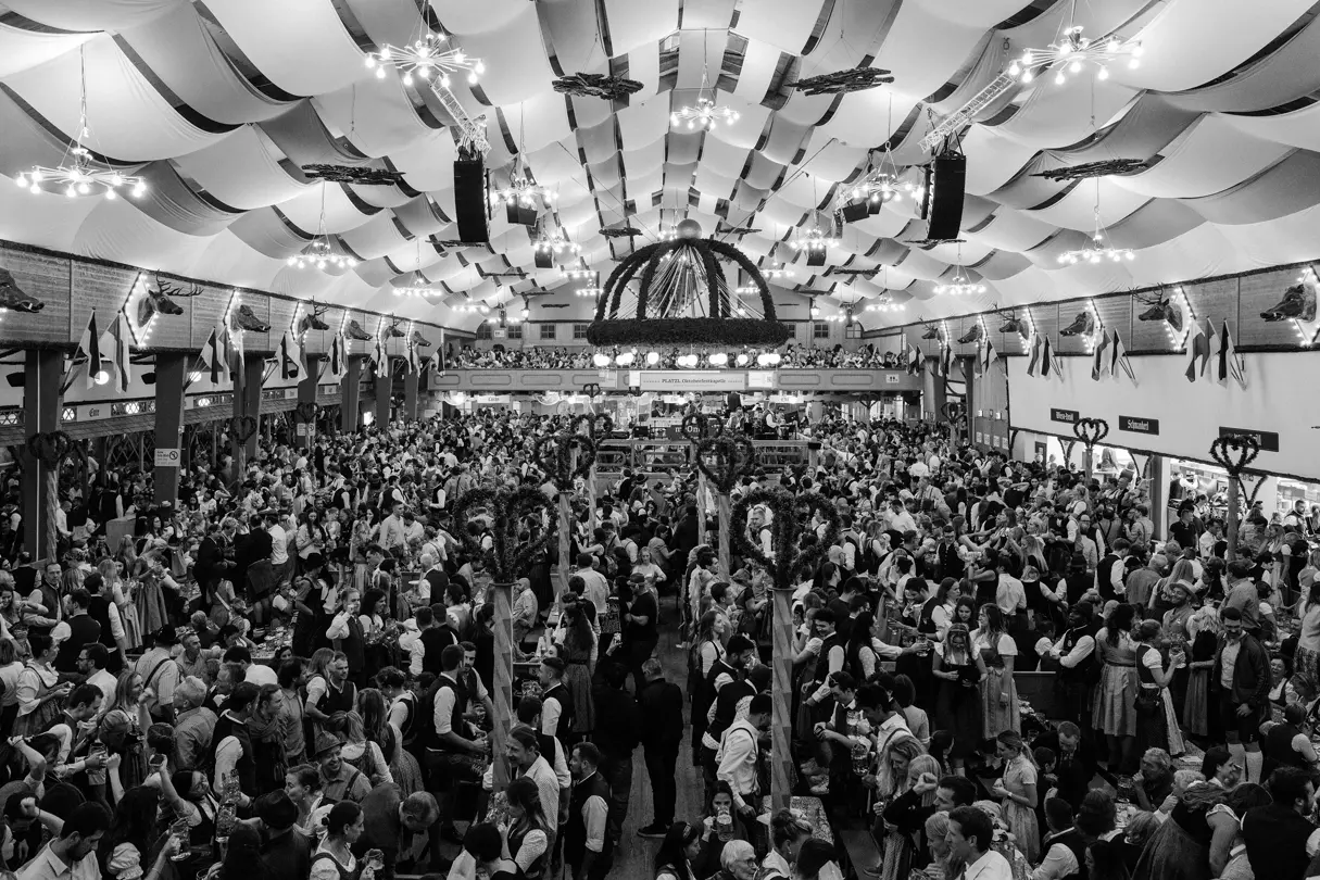 Packed beer tent at Munich Oktoberfest with guests in traditional Bavarian attire celebrating beneath festive decorations.