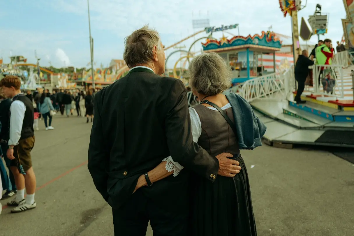 Older couple in traditional Bavarian clothing walking arm in arm through the Munich Oktoberfest fairground.