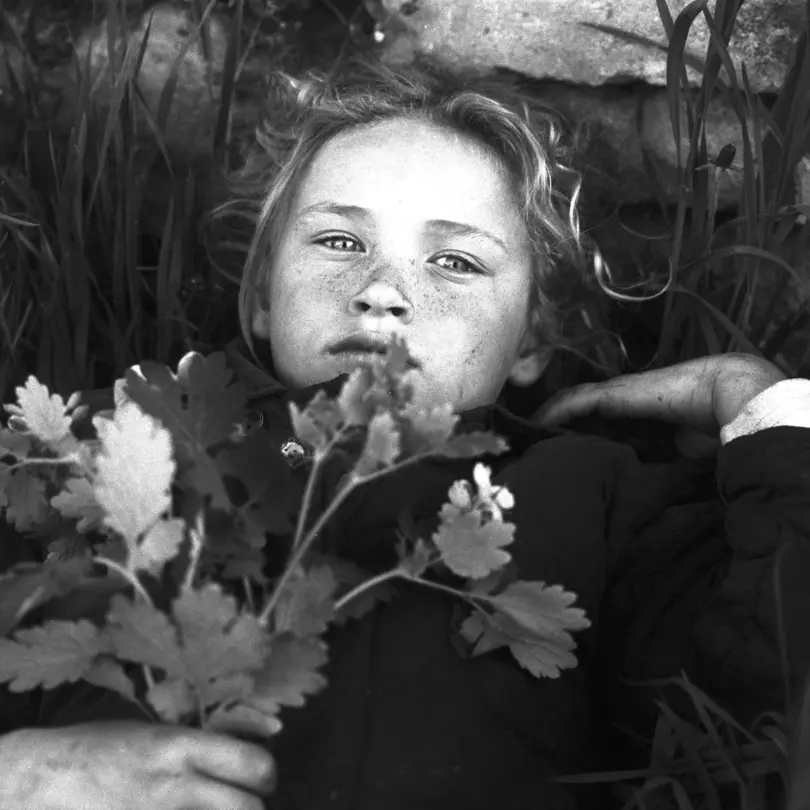 LOBA Newcomer 2024 image: Black-and-white portrait of a child lying in the grass holding wildflowers.