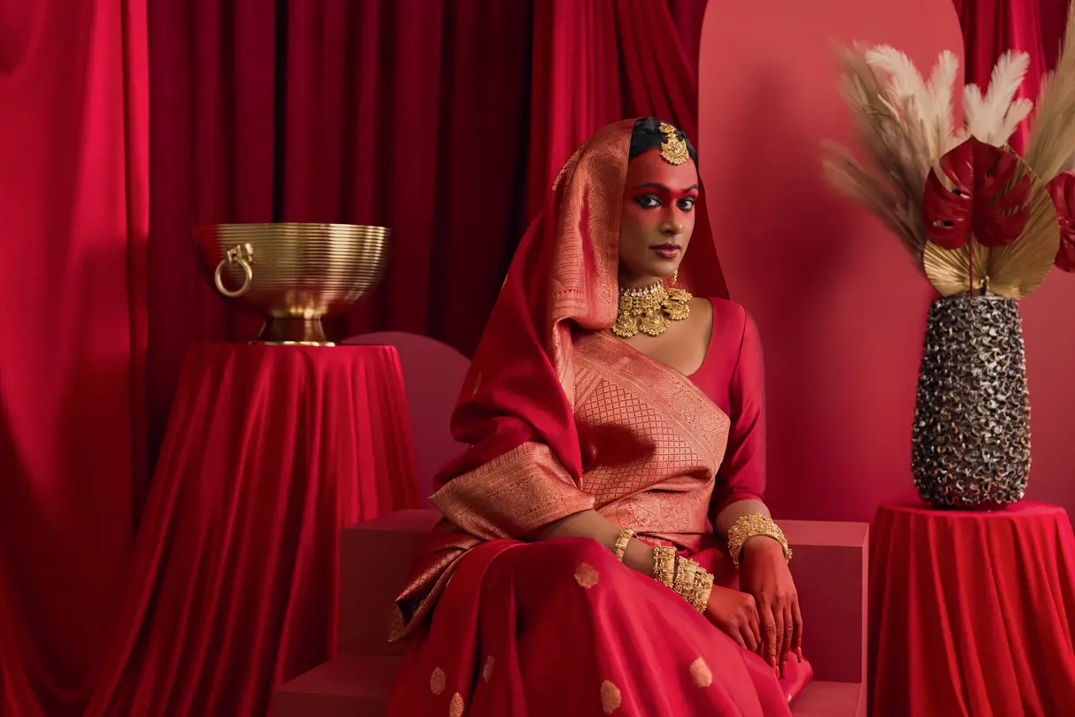 1. Portrait in red traditional attire — Seated portrait of a person wearing an elegant red and gold sari with ornate jewelry, surrounded by rich red drapery and decorative objects.