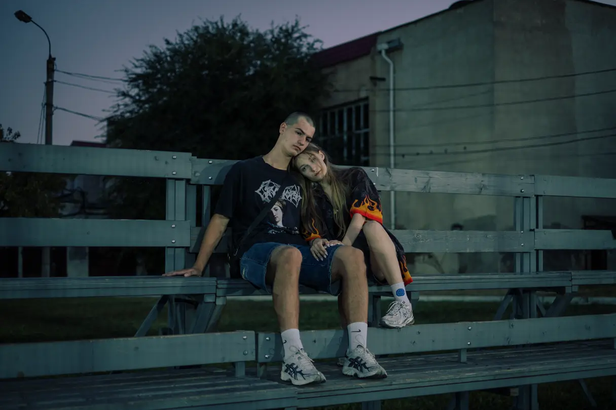 LOBA Newcomer 2025 image:Two young people sitting closely together on outdoor bleachers at dusk.