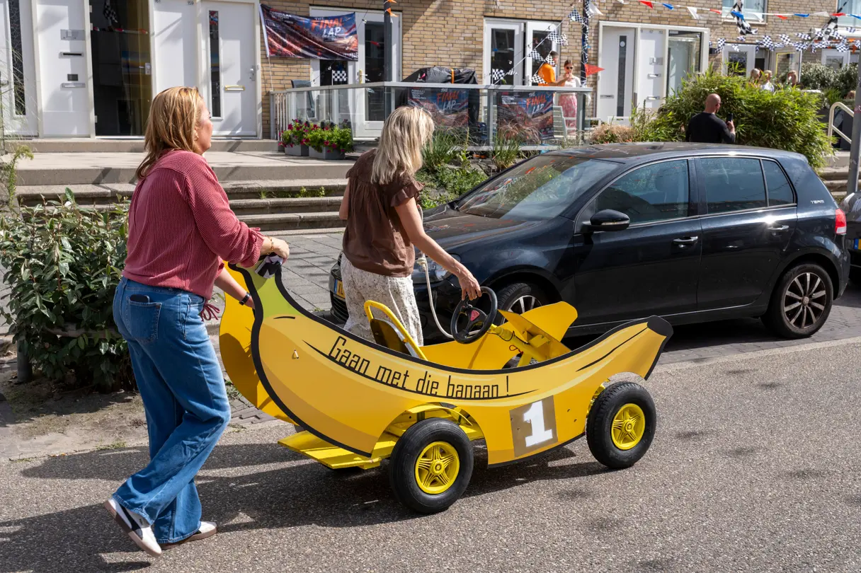 Two women push a playful yellow banana-shaped vehicle through a decorated street in Zandvoort during the Formula 1 Dutch Grand Prix.
