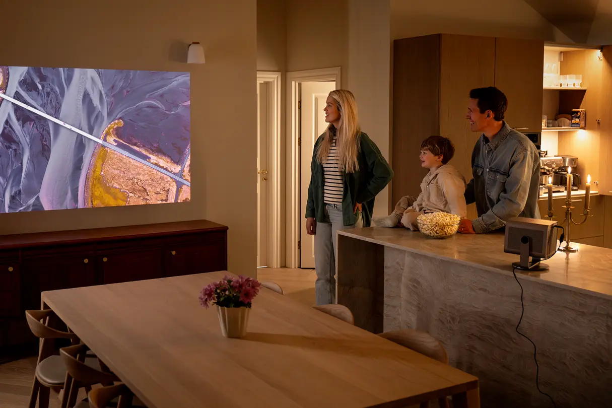 Three people standing in the dining room watching a Leica Cine Play 1 projection.