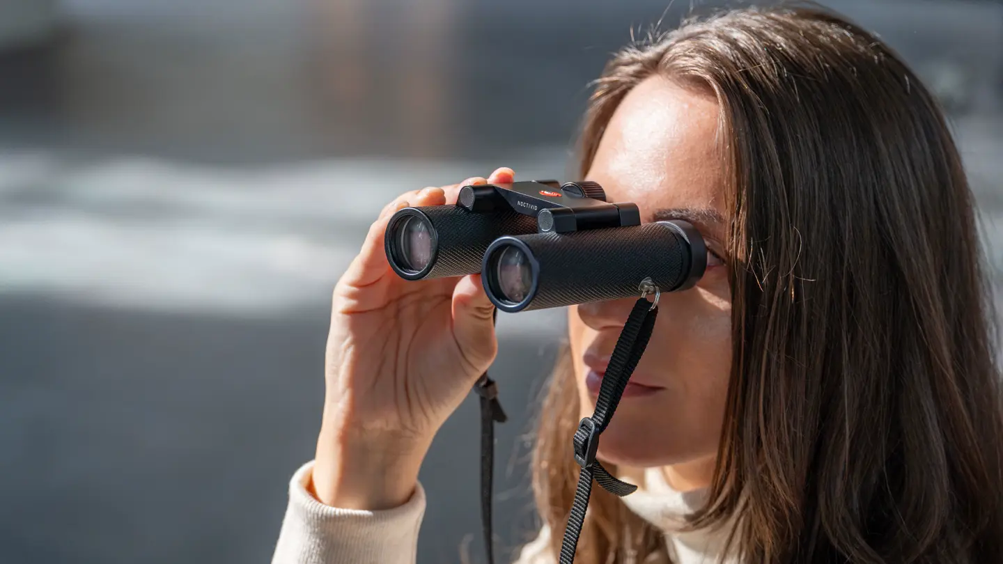 Woman using black Noctivid Compact binoculars to observe distant scenery