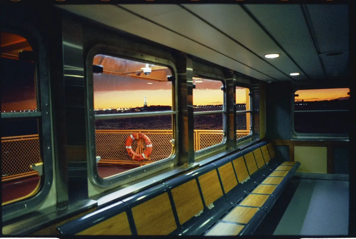 New York Harbor: View from inside a New York City ferry at sunset, with the Statue of Liberty visible through the windows across the harbor.