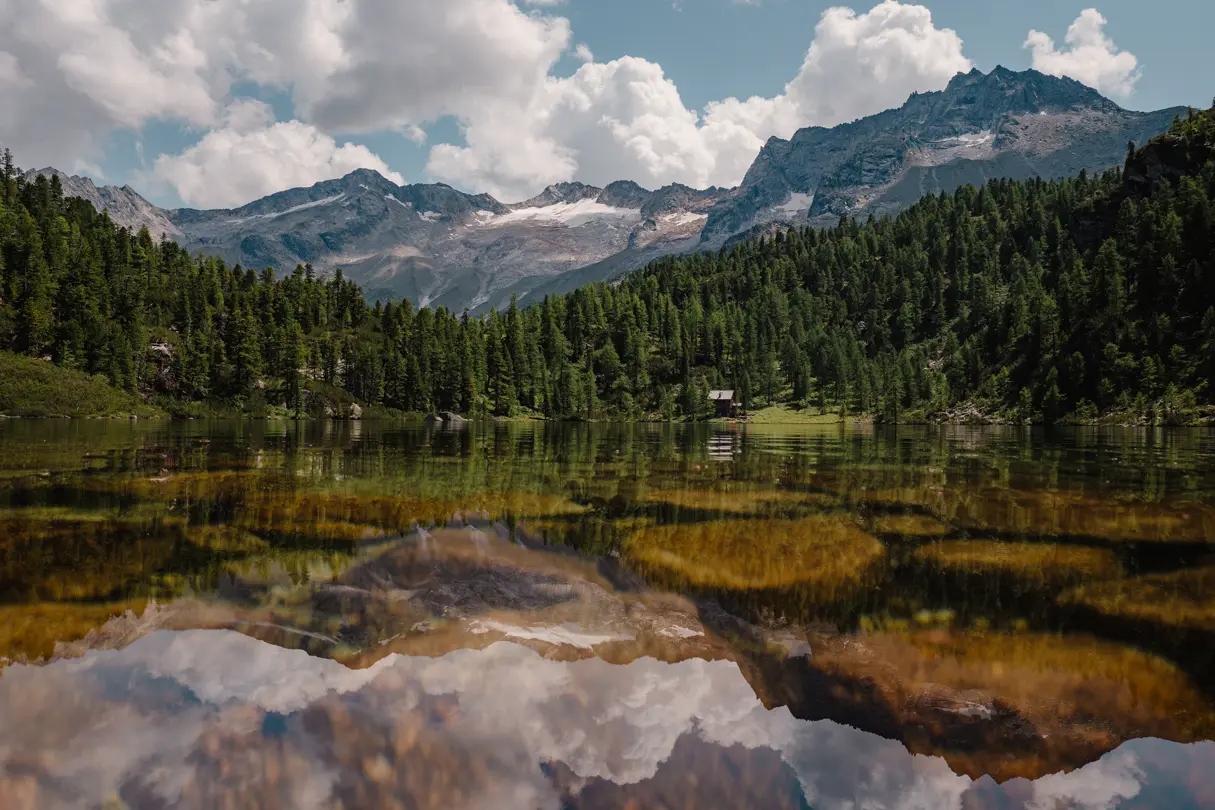 Alpine mountain lake — Clear mountain lake reflecting dramatic peaks, forest and summer clouds in a tranquil Alpine landscape.
