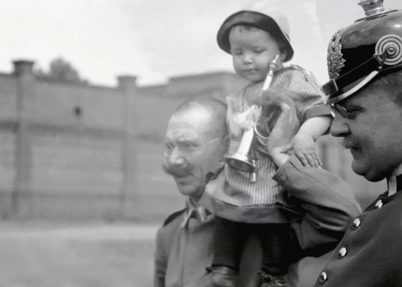 Historic black-and-white photograph of a uniformed policeman holding a small child, with another man walking alongside them.