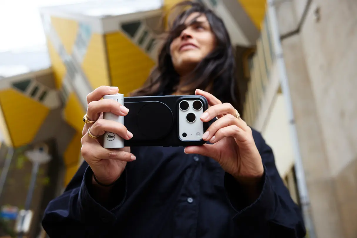 Woman holding a smartphone with a white Leica LUX grip in a modern indoor setting