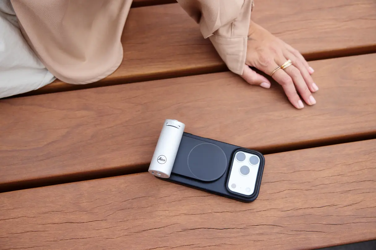 Leica LUX camera grip attached to a phone on a wooden bench beside a seated person
