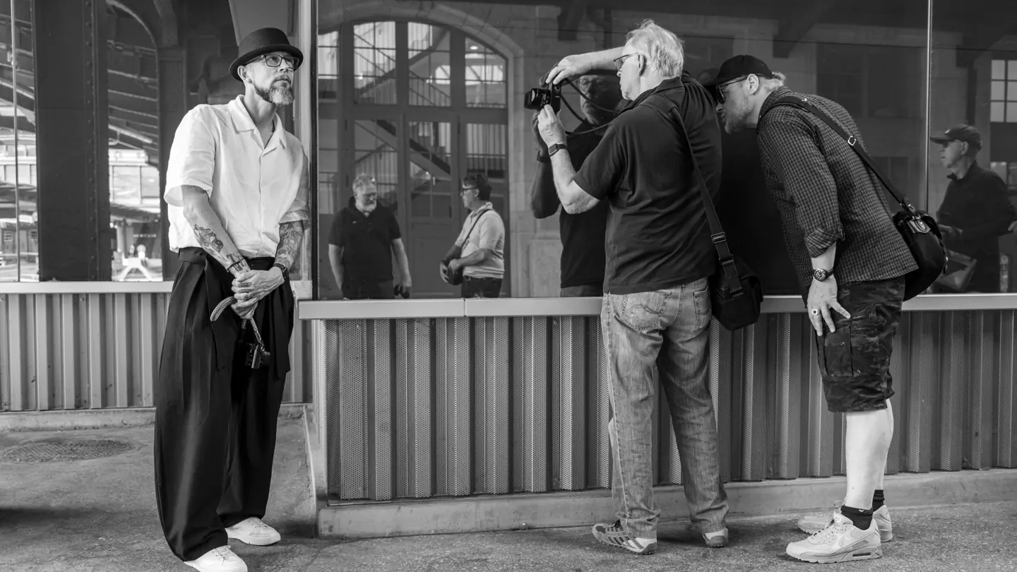 A photographer takes a portrait of a man in a hat while another participant observes.
