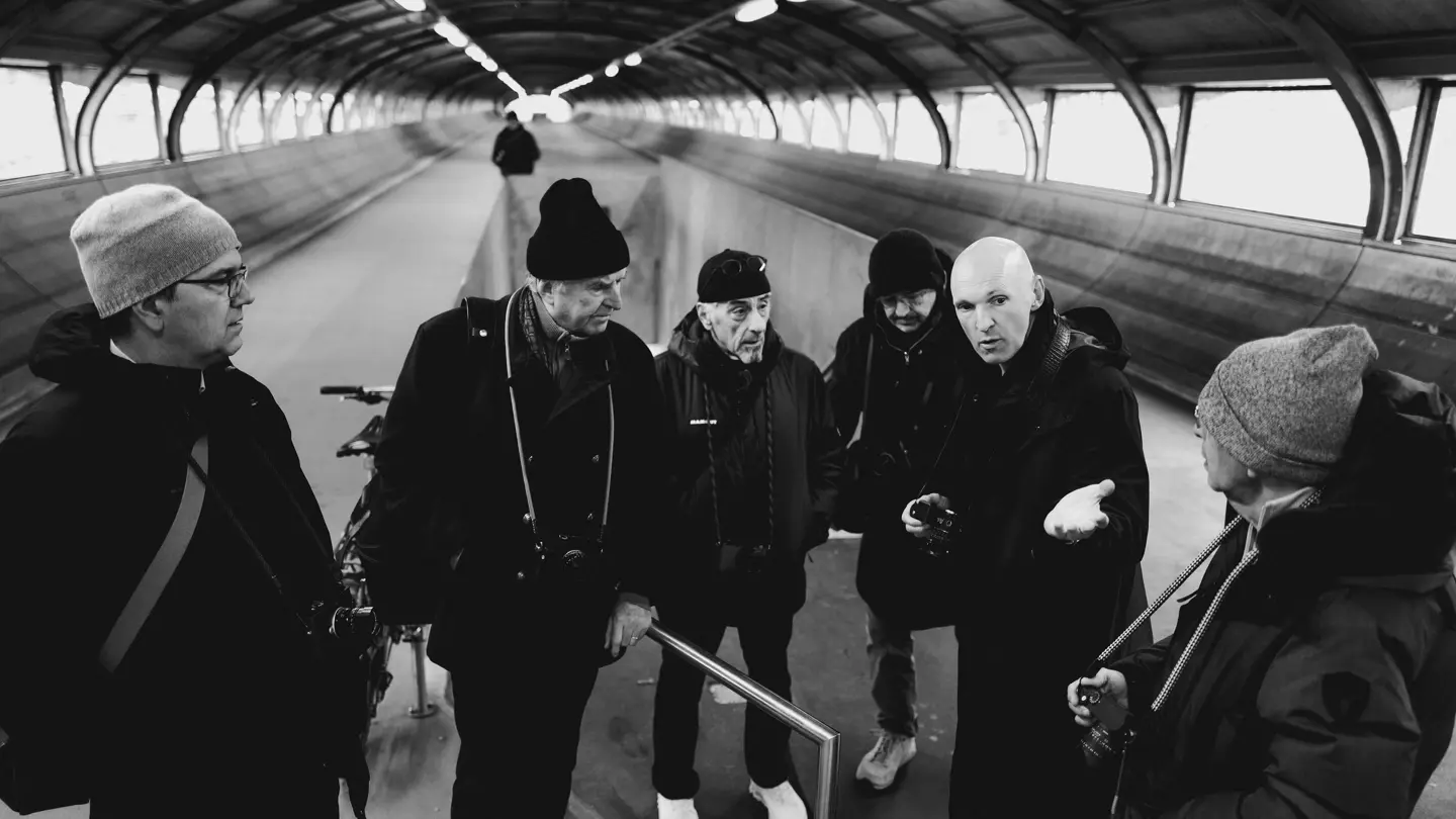 A black-and-white photograph of a group of photographers discussing photography inside a covered pedestrian tunnel.