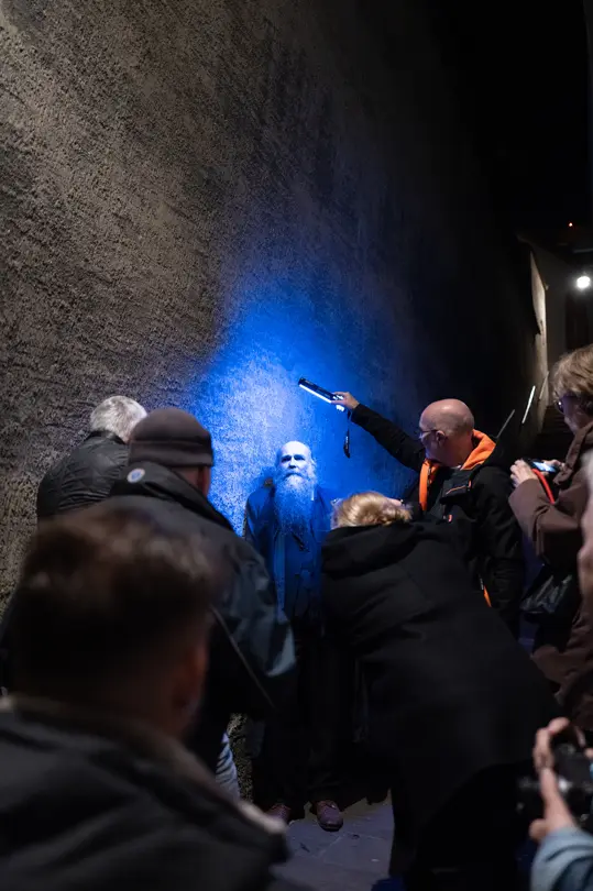 Photographers capture a portrait of a bearded man illuminated by blue light against a textured wall.