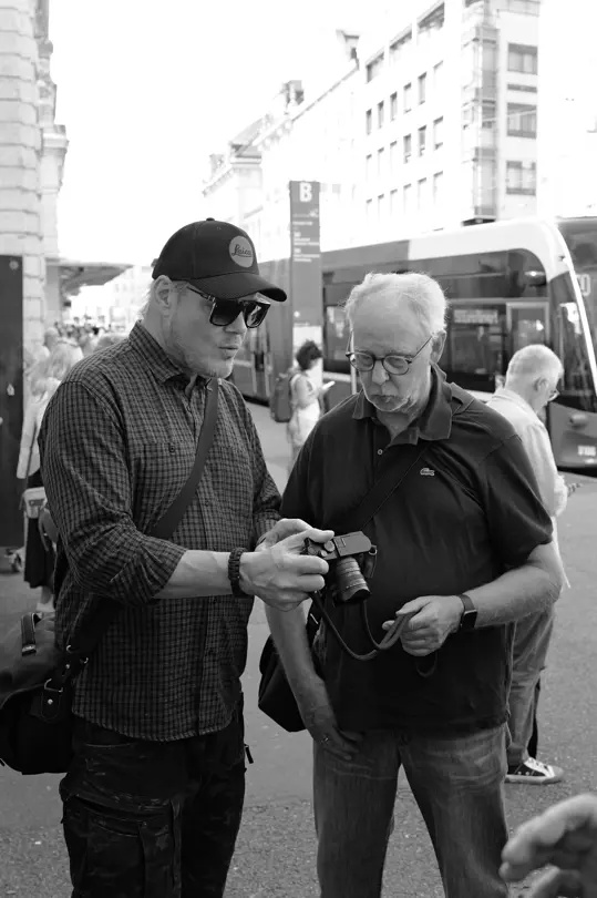 Two photographers review images on a Leica camera during a street photography workshop.