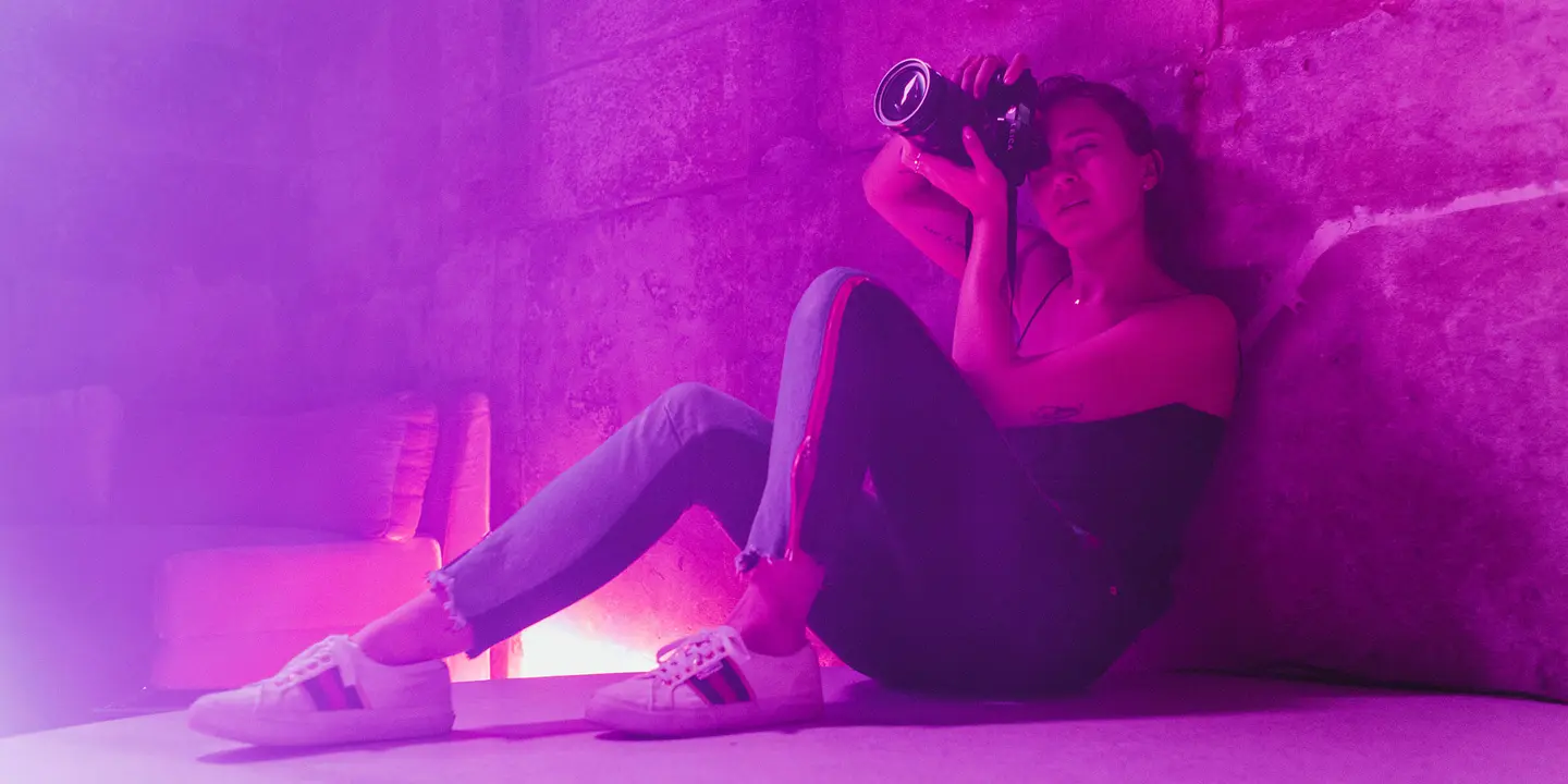 Alex Drewniak sits on the floor, taking pictures in a room lit by pink-purple light.