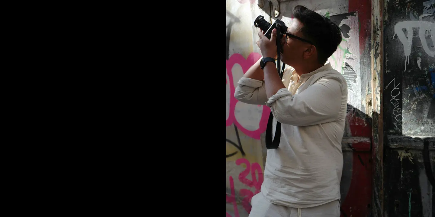 Patrick Domingo takes a photo standing in front of a graffiti wall.