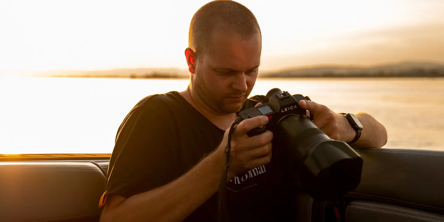 Tino Scherer looking at his camera. In the background is a sea at sunset.