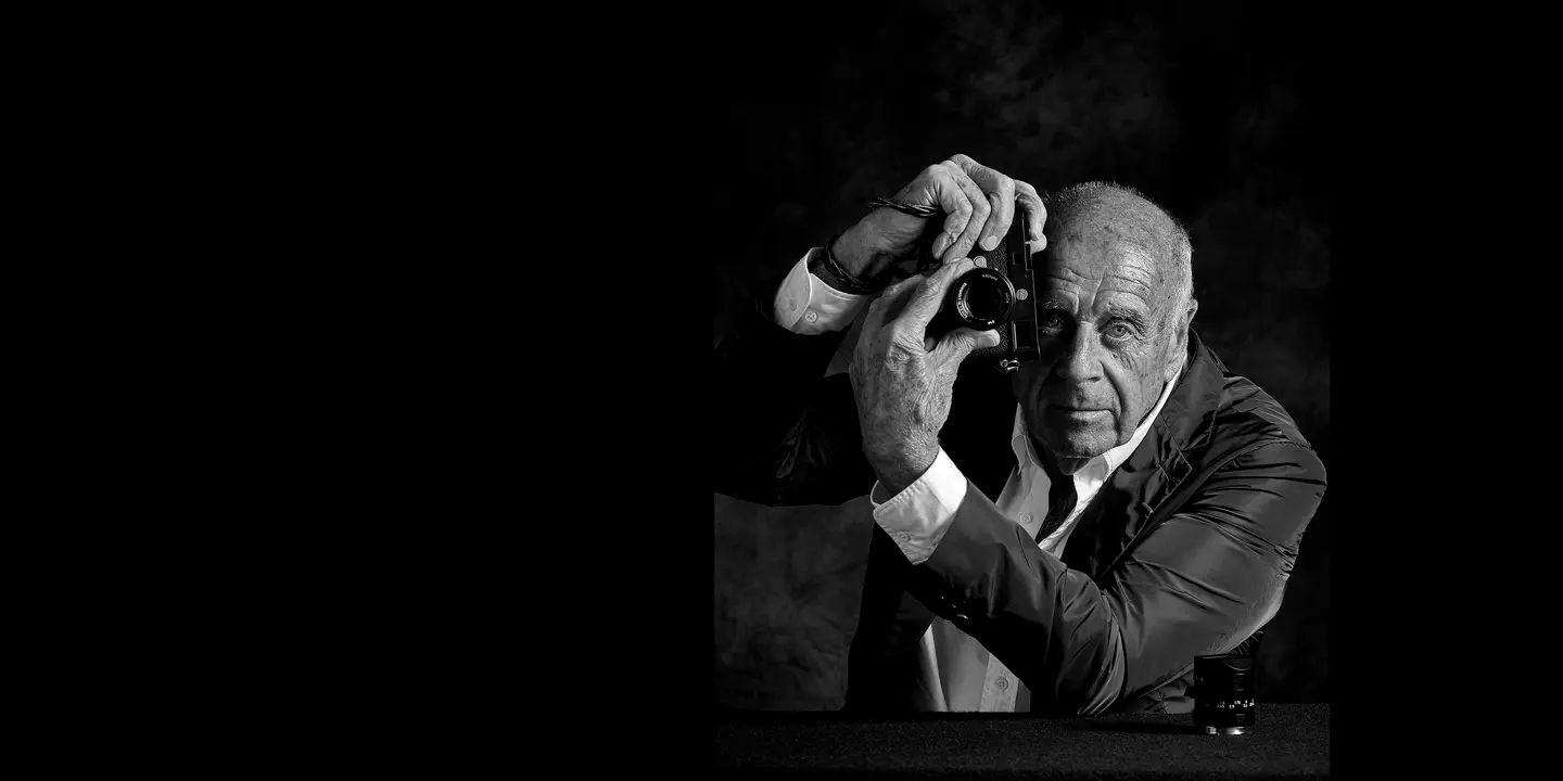 Elderly man holds a camera in front of his face and turns the lens of the camera.