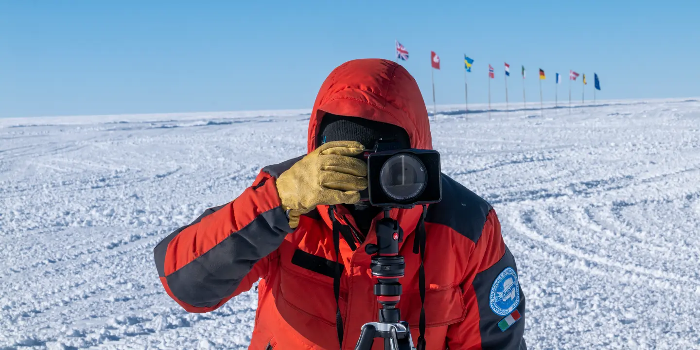 Person takes a photo in a snowy landscape with European flags in the background.