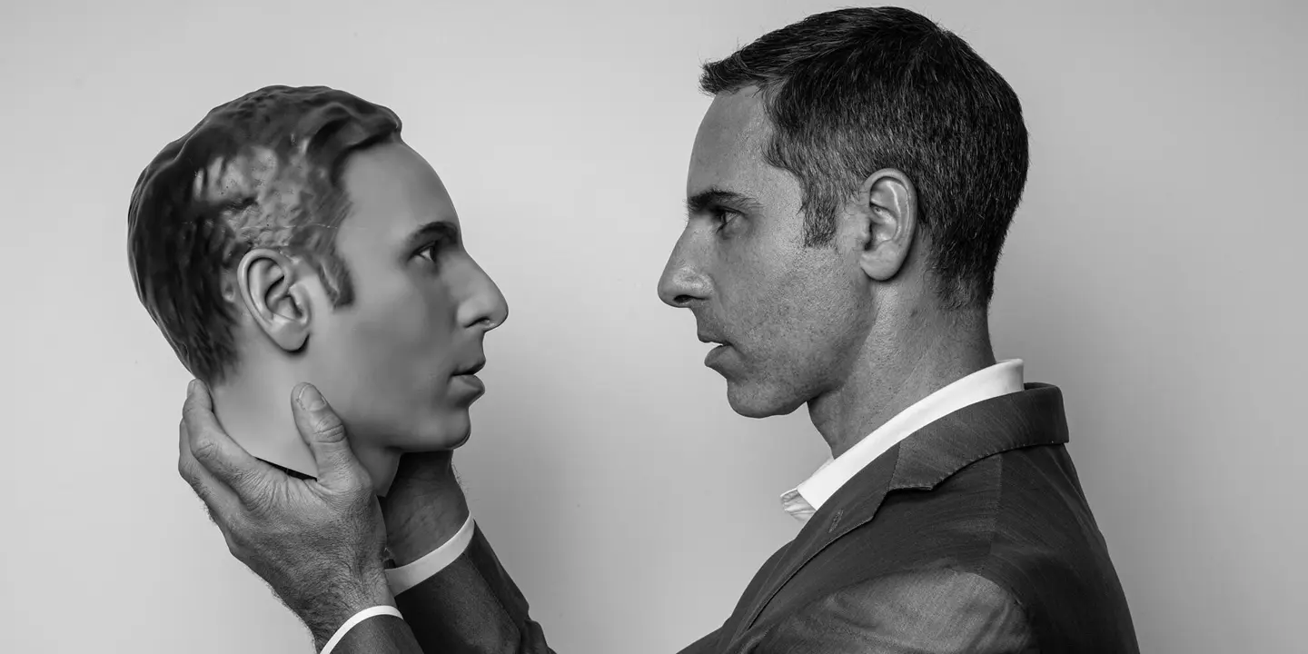 A man holds an artificial head in his hands and looks directly into its eyes.