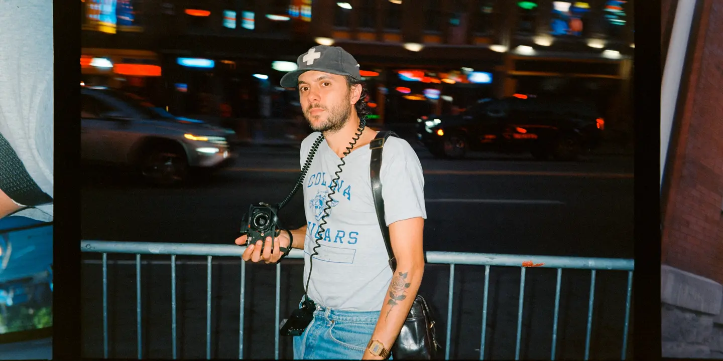 Joe Greer with a Leica M6 in his hand standing at a street at night.