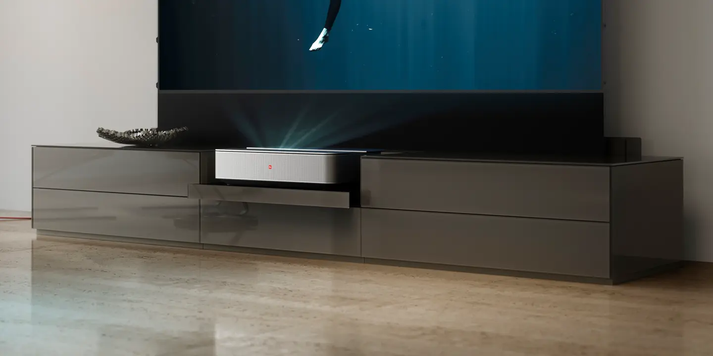 A Leica projector in a gleaming TV cabinet in a living room projects an image onto a screen.