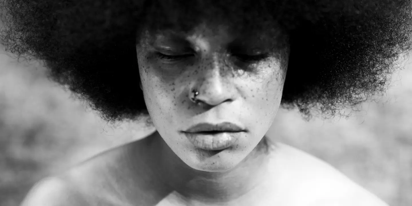 A close-up of a person with closed eyes and Afro hairstyle in black and white