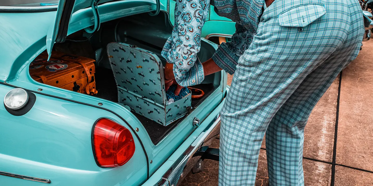 A person packs suitcases into the trunk of a turquoise vintage car.
