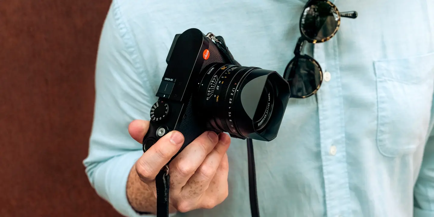 A man wearing a blue shirt holding a Leica camera in his right hand