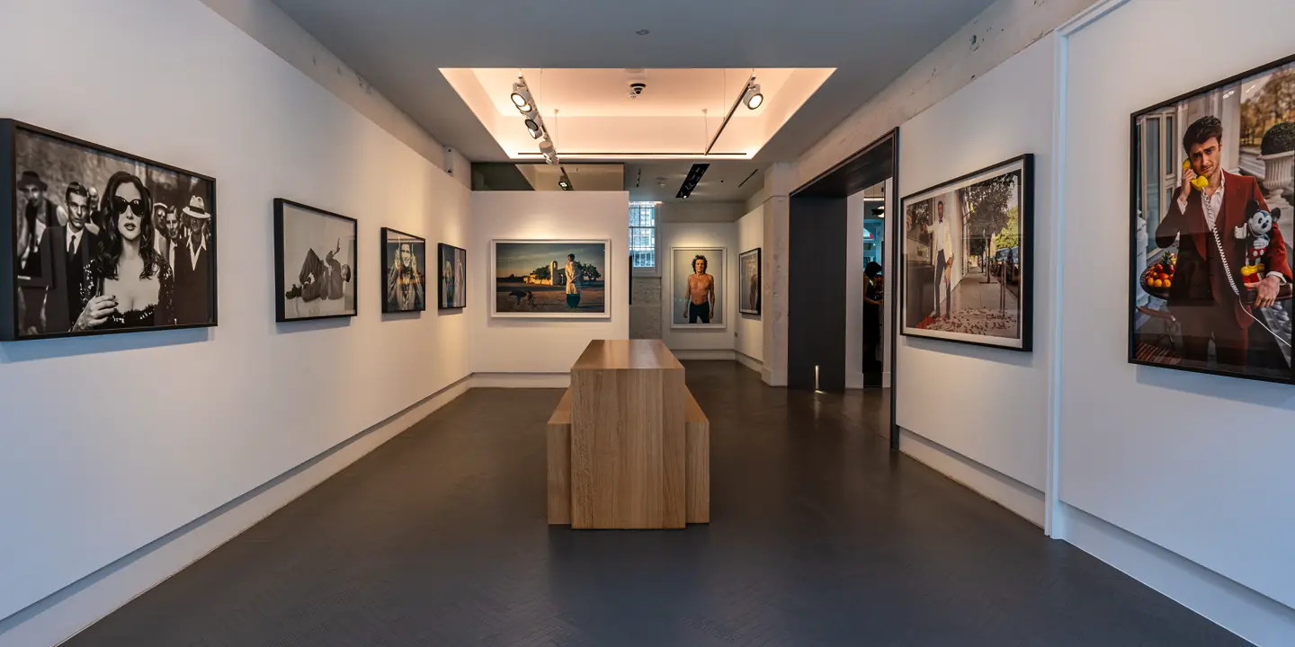 Exhibition room with photographs of various people and a wooden counter and benches in the centre of the room.