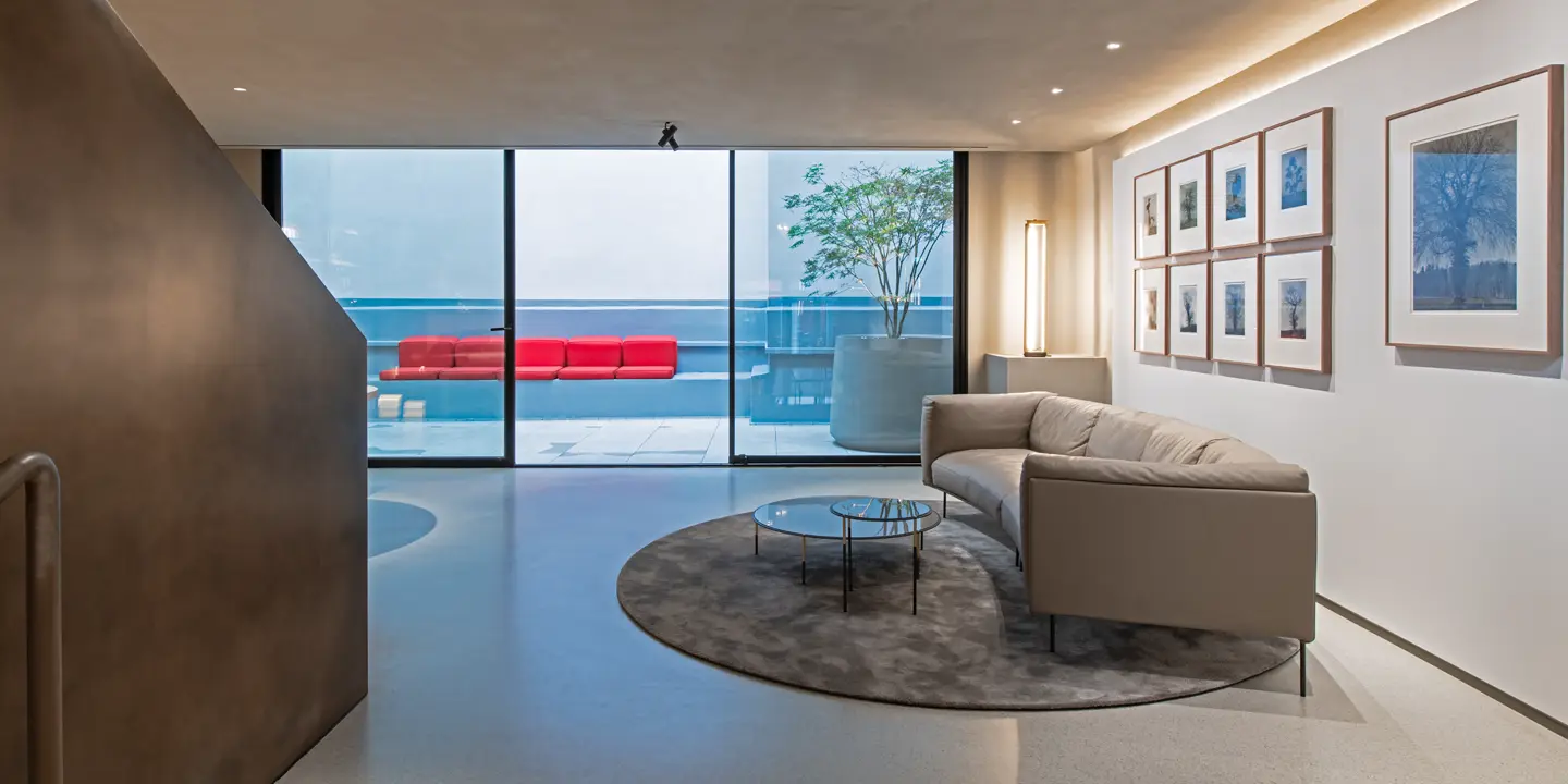 Modern room with sofa, glass table, photographs of trees and view of terrace with red seats.