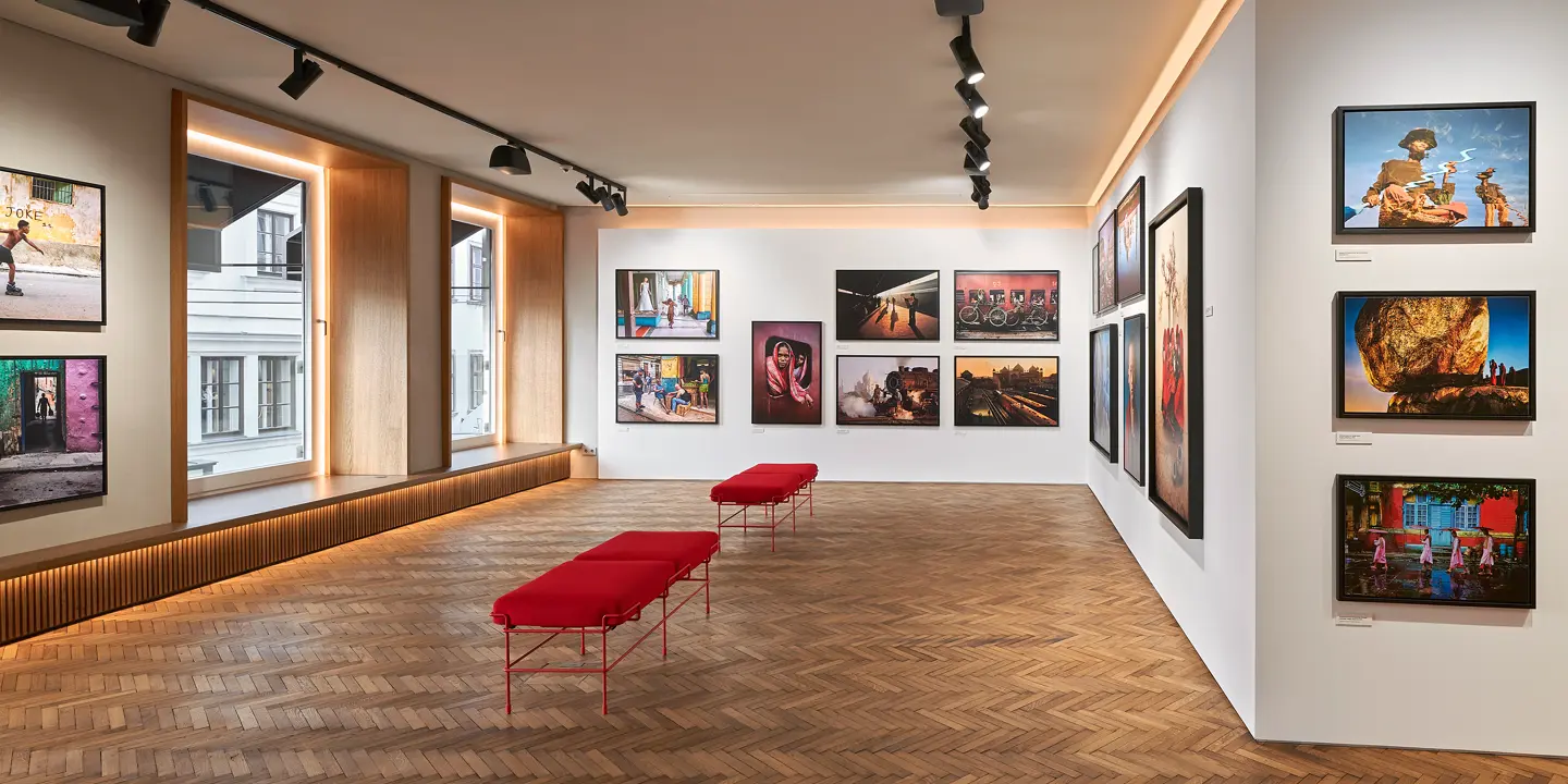 Exhibition space with red benches and photographs of people and places from all over the world.