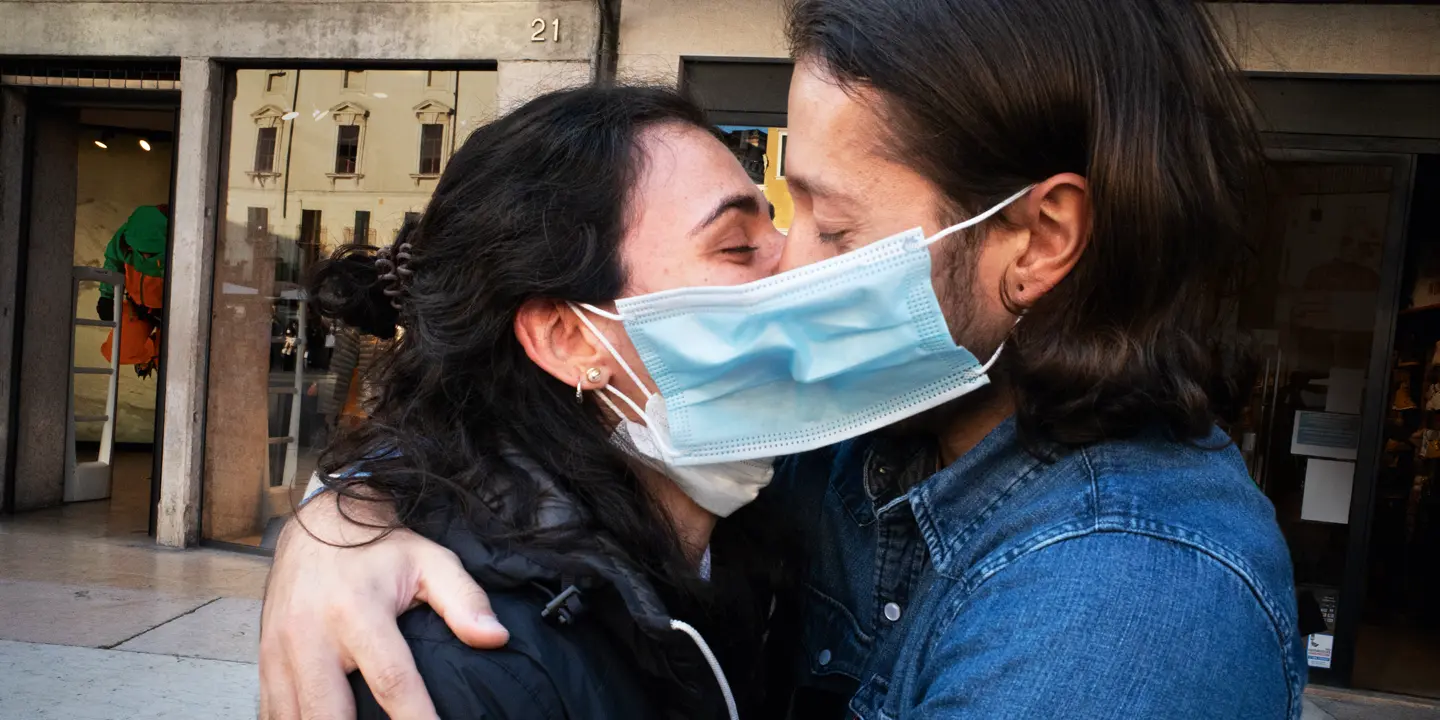 A couple wearing face masks hug and kiss in a street