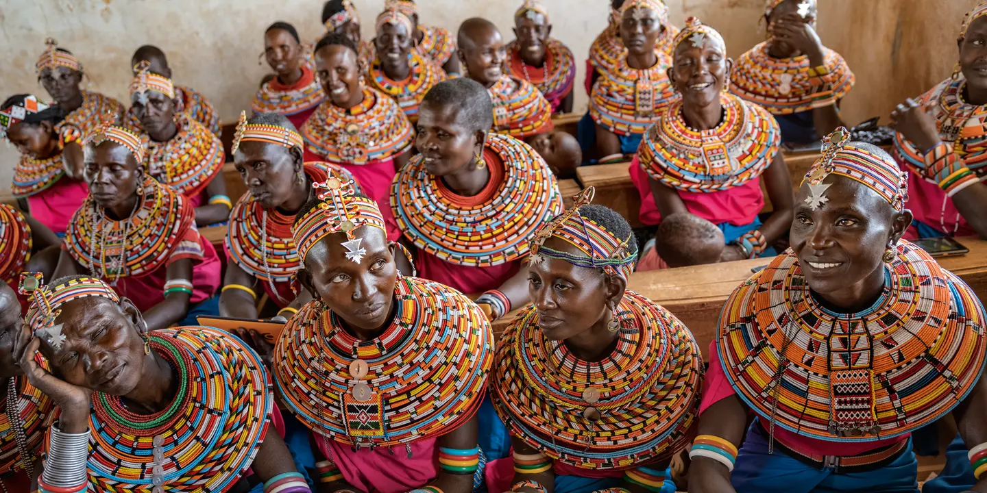 Women from the Samburu tribe in Kenya sitting on a wooden bench in traditional clothes and smiling.