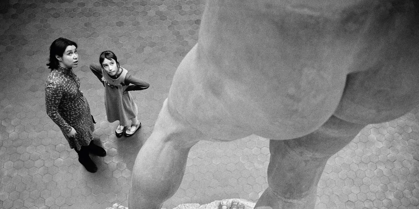 Two people stand in front of a large statue and look upwards.