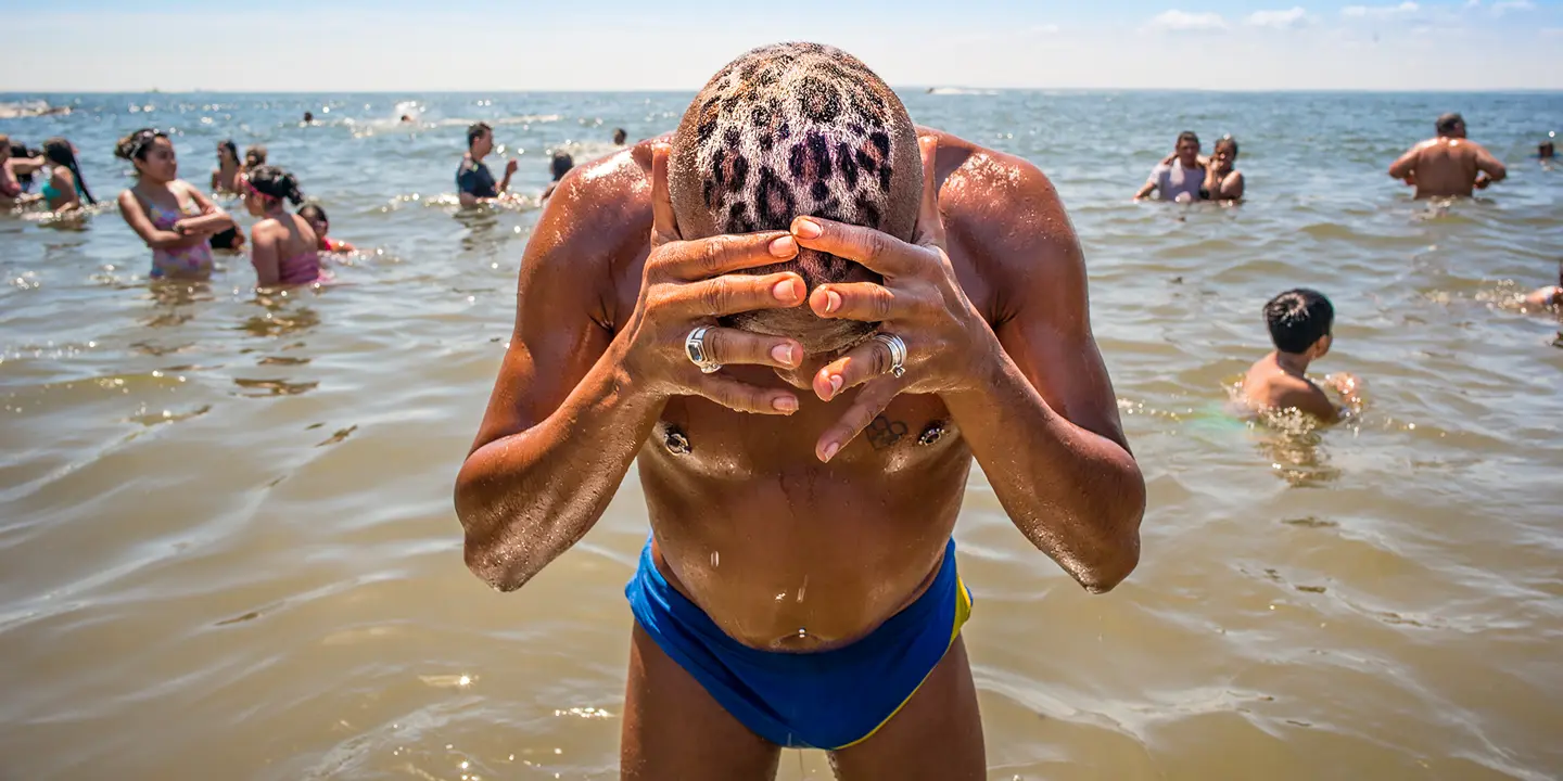 A man with a leopard print on his head is standing in the water. Several people are bathing in the sea around him.