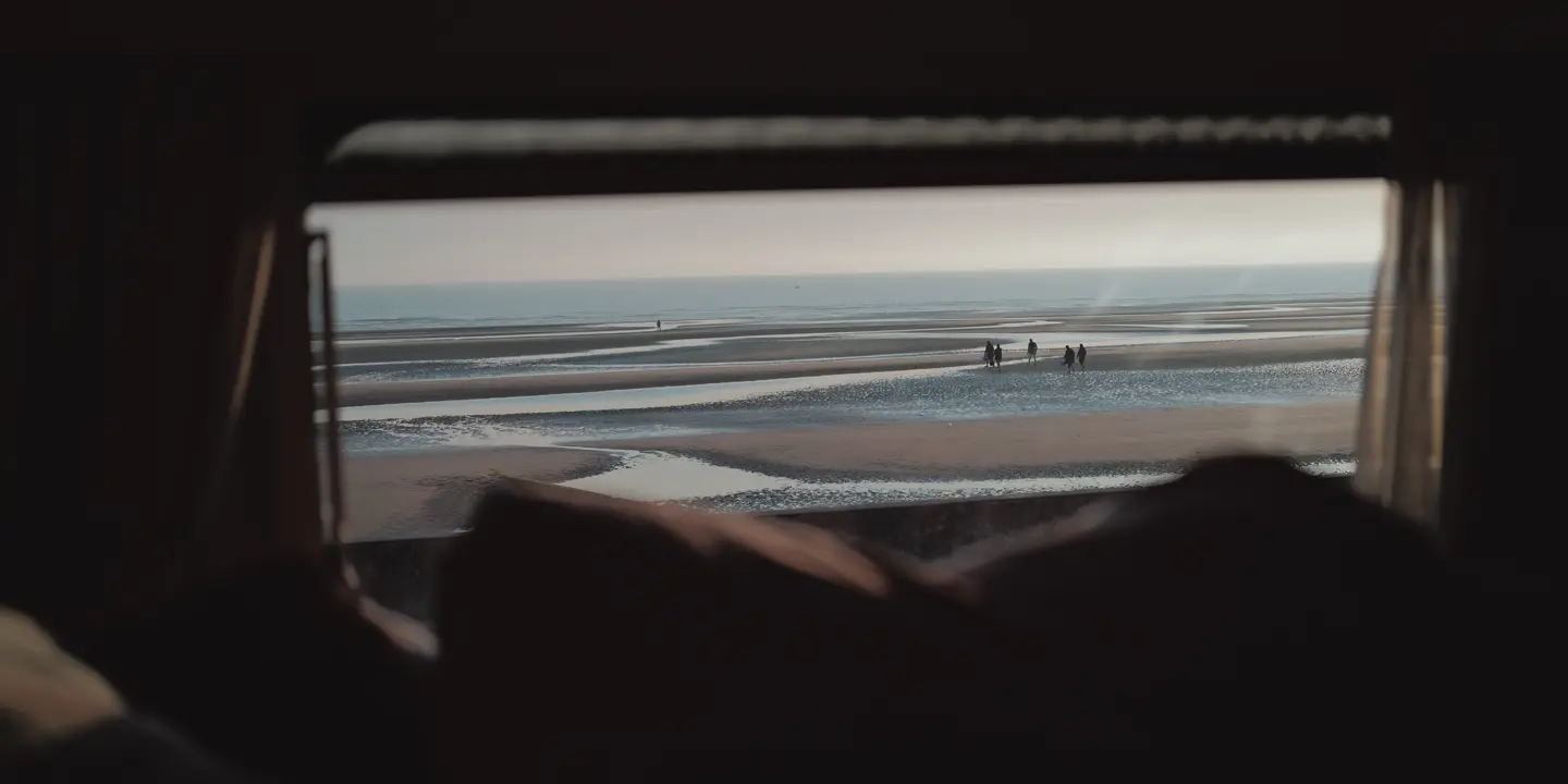 People on the beach photographed from a small window of a caravan