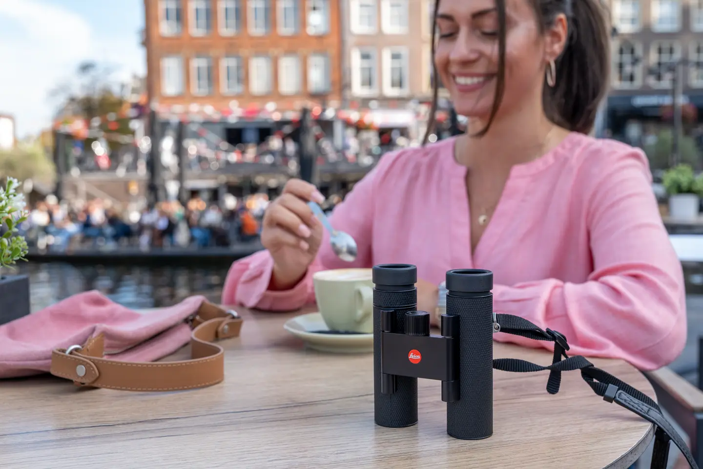 Woman is sitting in a cafe with her Leica Noctivid Compact next to her