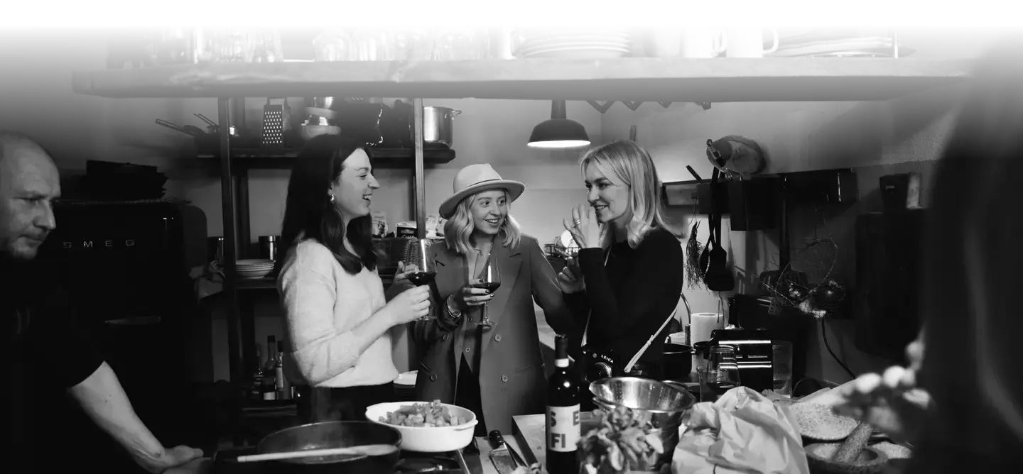 Three women with a wine glass in their hands stand in a kitchen