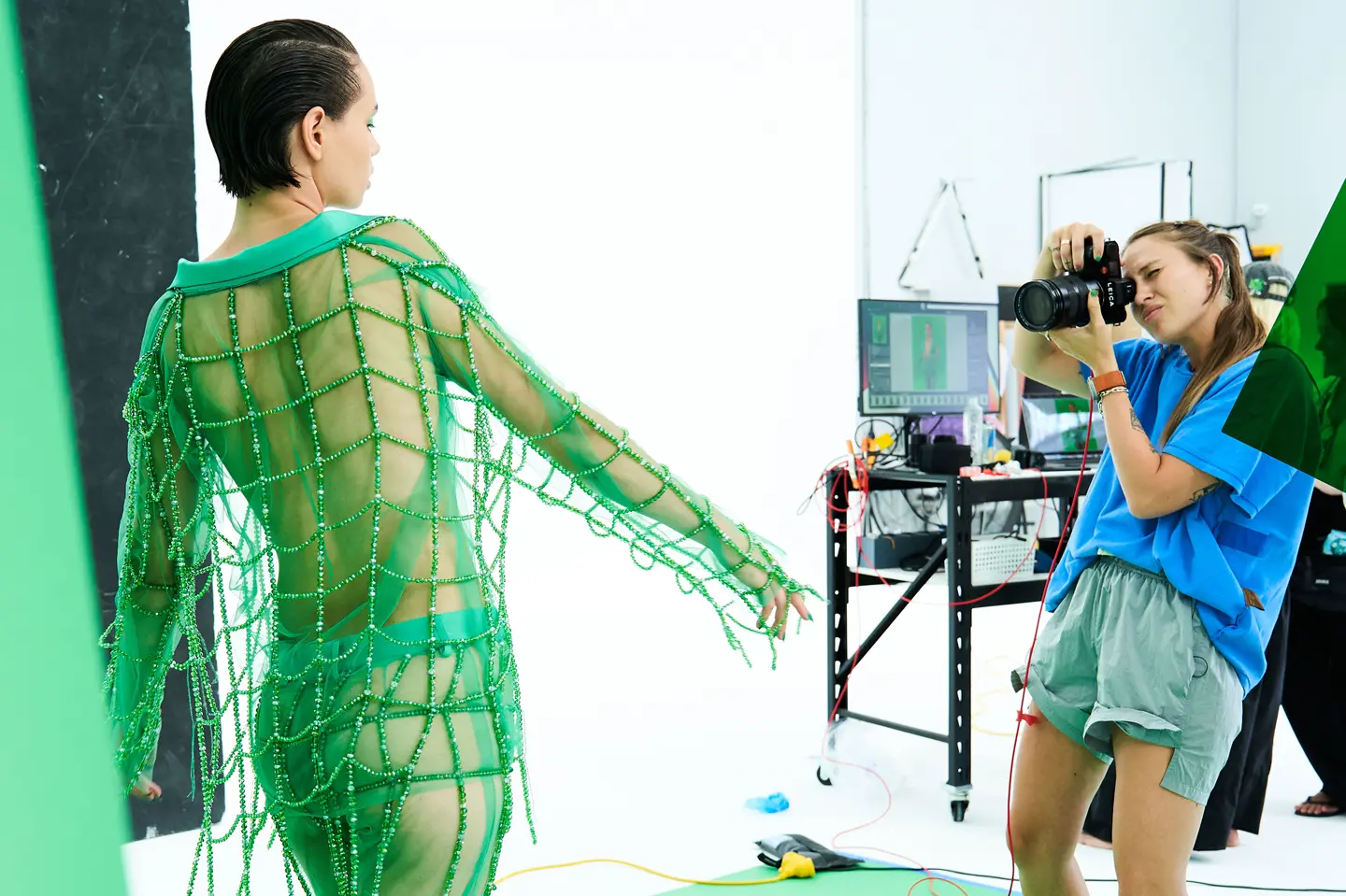 Photographer takes a picture in a studio of a model in a green net outfit.